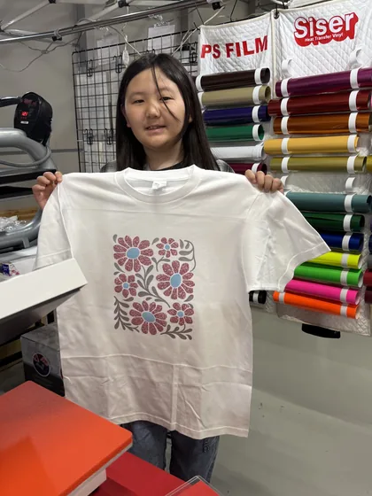 完成した花柄デザインのTシャツを広げて見せる参加者