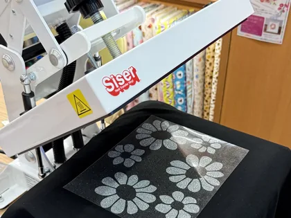 プレス機で黒いTシャツに花柄デザインを圧着する様子